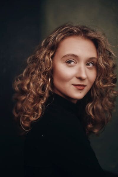 A portrait of Camille in a black turtleneck, her eyes are directed to the far left of the image.